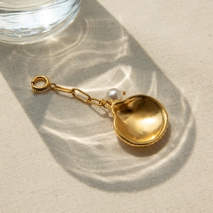 Pendentif coquille dorée avec perle et fermoir à ressort sur fond beige texturé