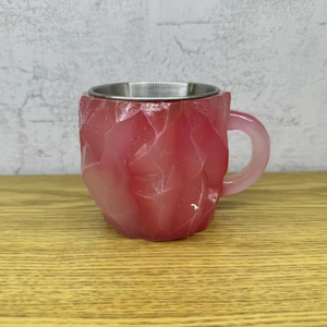 Detailed view of a red crystal resin coffee mug with a metal liner on a wooden table
