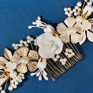 Close-up of golden bridal hair comb with white ceramic flowers and delicate pearls