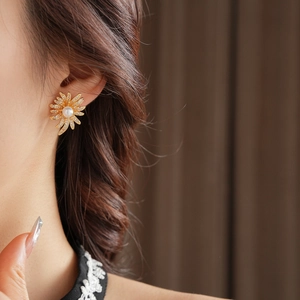 Macro view of gold sunflower stud earrings featuring a central pearl and zircon petals