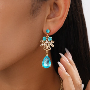 Close-up of elegant gold drop earrings with blue crystal and hollow flower design