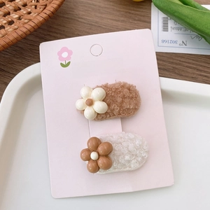 Close-up of plush floral hair clips in beige and brown wool on a fashion display card
