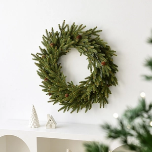 Christmas wreath with artificial pine needles and small pinecones on a white wall
