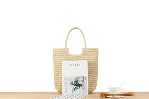 Detailed close-up of a woven straw tote bag with a U-shaped handle on a wooden table