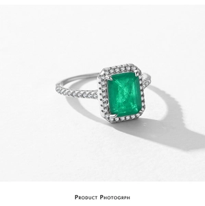 Macro shot of silver ring with emerald-cut green stone and pave diamonds on white