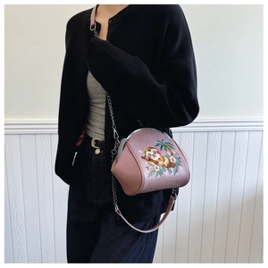 Pink shell bag with sloth embroidery and metal chain strap shown on a model