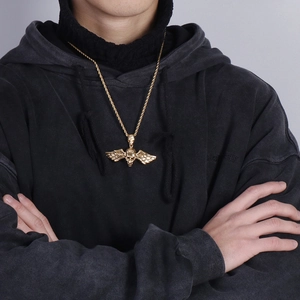 Détail d'un collier avec pendentif crâne ailé doré porté sur un sweat à capuche noir