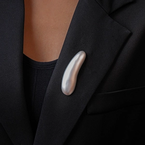 Silver satin finish bean-shaped brooch pinned on a black tailored blazer lapel