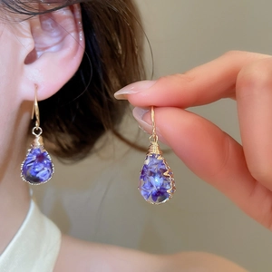 Detailed view of handmade teardrop resin earrings featuring purple dried flowers and gold hooks