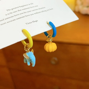 Detail of gold hoop earrings featuring blue elephant and orange pumpkin enamel charms