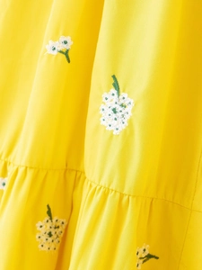Close-up of yellow cotton fabric with white floral embroidery and ruffled hem detail