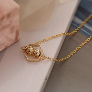 Close-up of golden necklace featuring a hexagonal pendant with two engraved beads