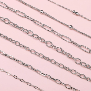 Selection of stainless steel jewelry chains including cable and bead styles on pink background