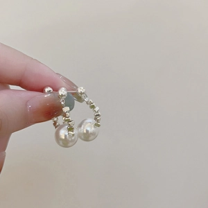Detailed close-up of a silver pearl hoop earring held by hand against a soft beige background