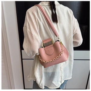 Pink leather bucket bag with gold circular handle and chain strap worn by a model