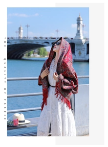 Outdoor lifestyle photo of red paisley shawl with tassels worn by model near a bridge