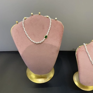 Pink velvet jewelry bust featuring a white pearl necklace with emerald green pendant