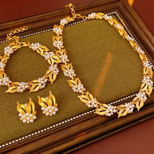 Vintage jewelry set with gold leaf patterns, pearls, and zircons on a dark green surface