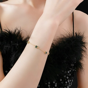 Détail d'un bracelet doré avec des zircons carrés verts porté au poignet d'un mannequin