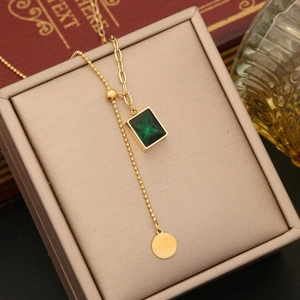 Macro detail of gold necklace with rectangular emerald green gemstone and round charm