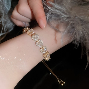 Detail of adjustable gold heart bracelet with clear zircons on a soft feather background