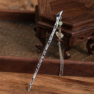 Detailed close-up of a silver bamboo-style hair pin with elegant green tassel and fan