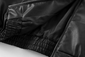 Detailed macro view of black faux leather aviator jacket showing texture and elastic hem