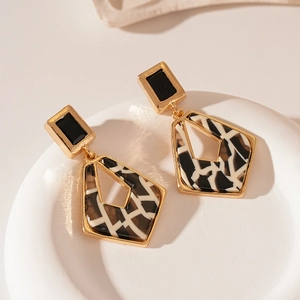 Detail of geometric tortoise shell acetate earrings with gold trim on a white display tray