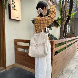 Detail of striped canvas tote bag with Bonjour embroidery and pleated texture on shoulder