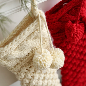 Cable knit Christmas stockings in off-white and red with pom-poms for festive fireplace decor