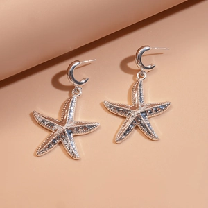 Macro detail of silver starfish drop earrings with textured relief and C-shape hoops