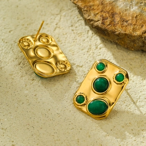 Detailed view of vintage gold textured earrings with green stones on natural stone background