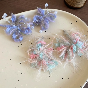 Detail view of handcrafted butterfly yarn earrings with pearls on a ceramic plate