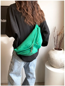 Detail of bright green nylon crossbody chest bag with silver zippers and wide strap
