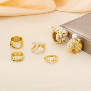 Set of six gold-plated rings with rhinestones, pearls, and crown designs on silk fabric