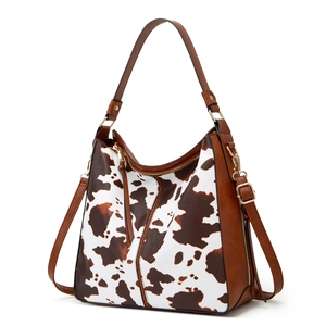 Detail of cow print tote bag with brown leather accents and golden hardware zippers