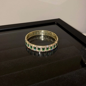 Macro shot of gold plated bracelet featuring green zirconia stones on black reflective stand