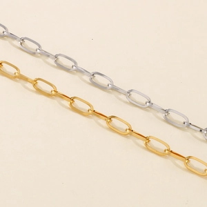 Detailed view of gold and silver square link paperclip chains on a beige surface