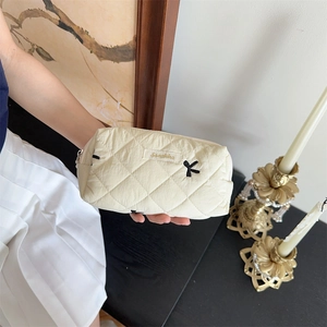 Detailed shot of beige quilted makeup bag with black bows and a gold zipper closure