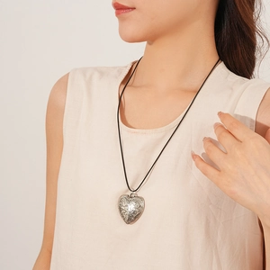 Close-up of a silver heart-shaped pendant with vintage vine relief on a black cord