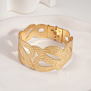 Dettaglio di un bracciale rigido dorato con trama a pelle di serpente e design traforato