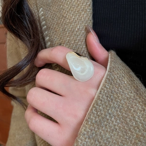 Gros plan d'une bague surdimensionnée en résine crème avec bordure dorée sur un doigt
