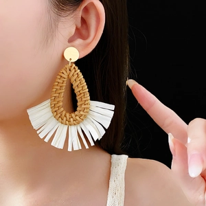 Detail of fan-shaped drop raffia earrings with white fringe tassels on model