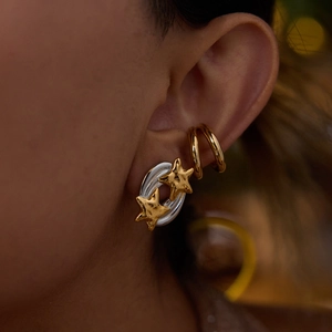 Close-up of star-shaped oval earrings and gold ear cuffs set on model ear detail
