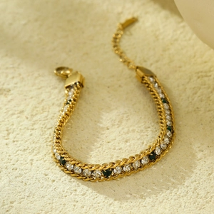 Elegant gold woven chain bracelet with green and white crystals on marble stone