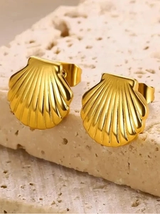 Macro shot of gold stainless steel shell earrings on textured white natural stone