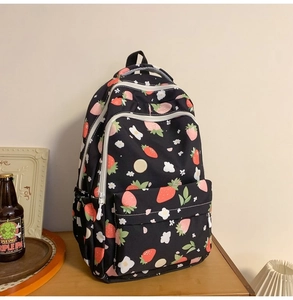 Detail of black strawberry print backpack showing multiple pockets on a wooden table