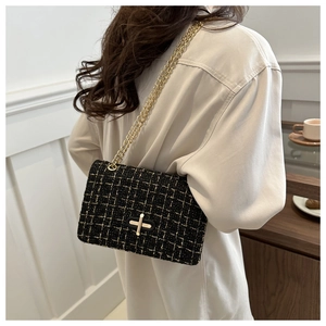 Elegant black and gold tweed crossbody bag with metal chain strap worn by a model