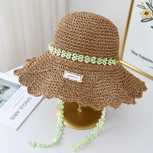 Detail of hand-woven straw hat with green floral lace trim on a gold metal stand