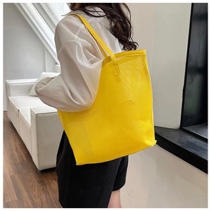 Detail view of large yellow mesh beach tote bag worn over the shoulder in indoor setting